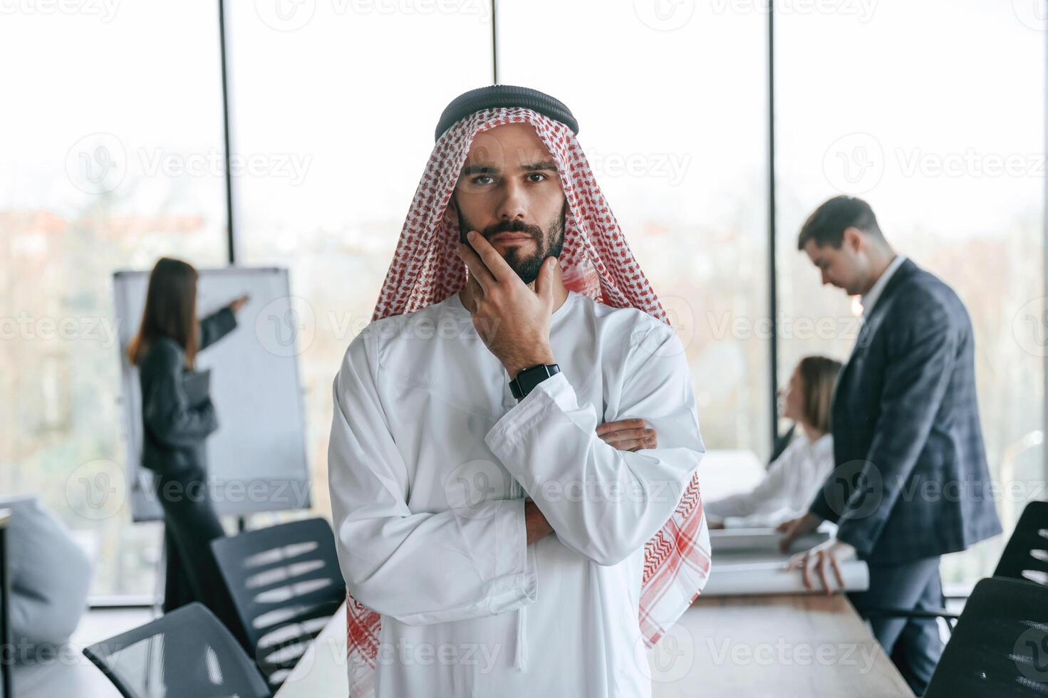 Standing in front of people that, behind... Muslim businessman in traditional outfit with colleagues in office photo