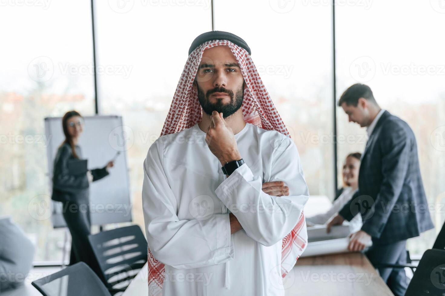 Standing in front of people that behind. Muslim businessman in traditional outfit with colleagues in office. photo
