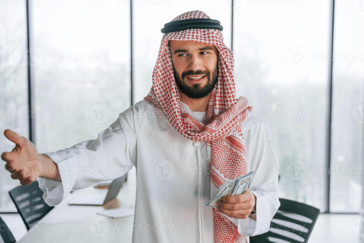 Holding money ,in hands. Successful ,Muslim businessman in traditional outfit in his office photo