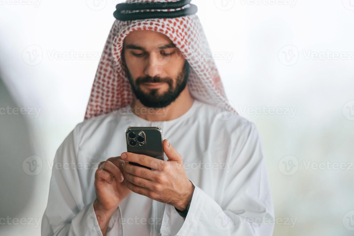 With ,smartphone in hand. Successful Muslim businessman in traditional outfit in his office photo
