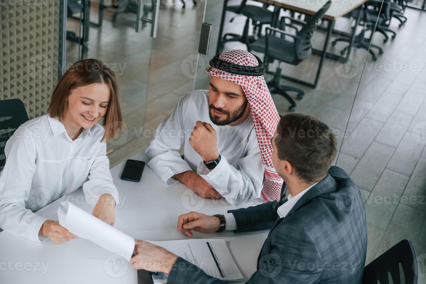 Sitting by the, table. Muslim businessman in traditional outfit with colleagues in office photo
