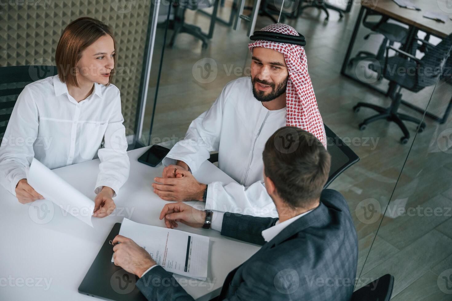 Sitting by, the table. Muslim businessman in traditional outfit with colleagues in office photo