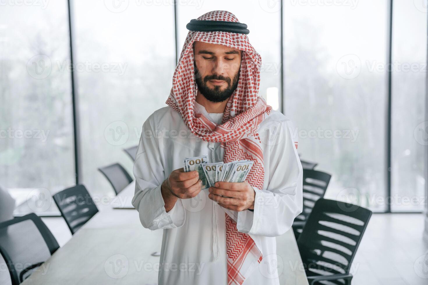 Holding,, money in hands. Successful Muslim businessman in traditional outfit in his office photo