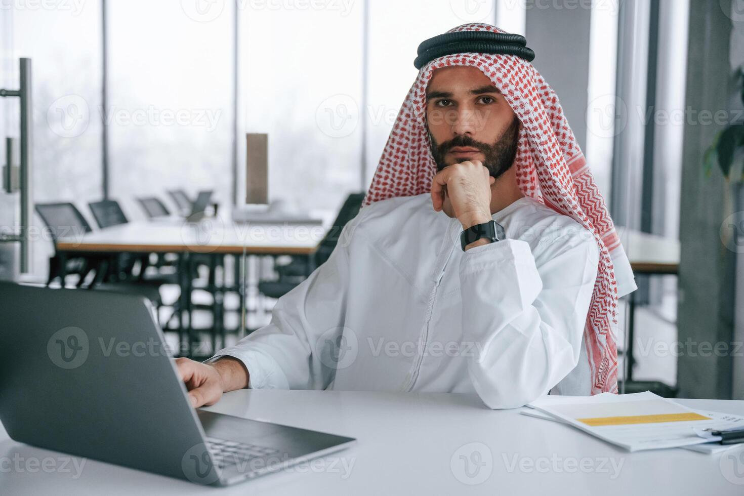 Working by, using laptop. Successful Muslim businessman in traditional outfit in his office photo
