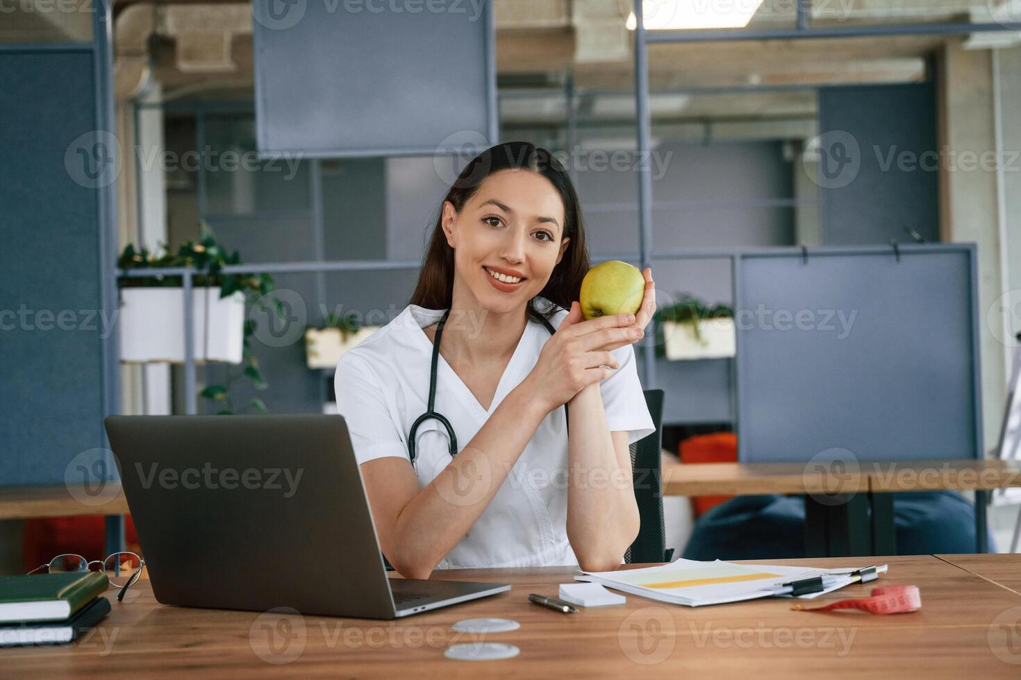 Nutritionist, with apple and laptop. Female doctor in white coat is indoors photo