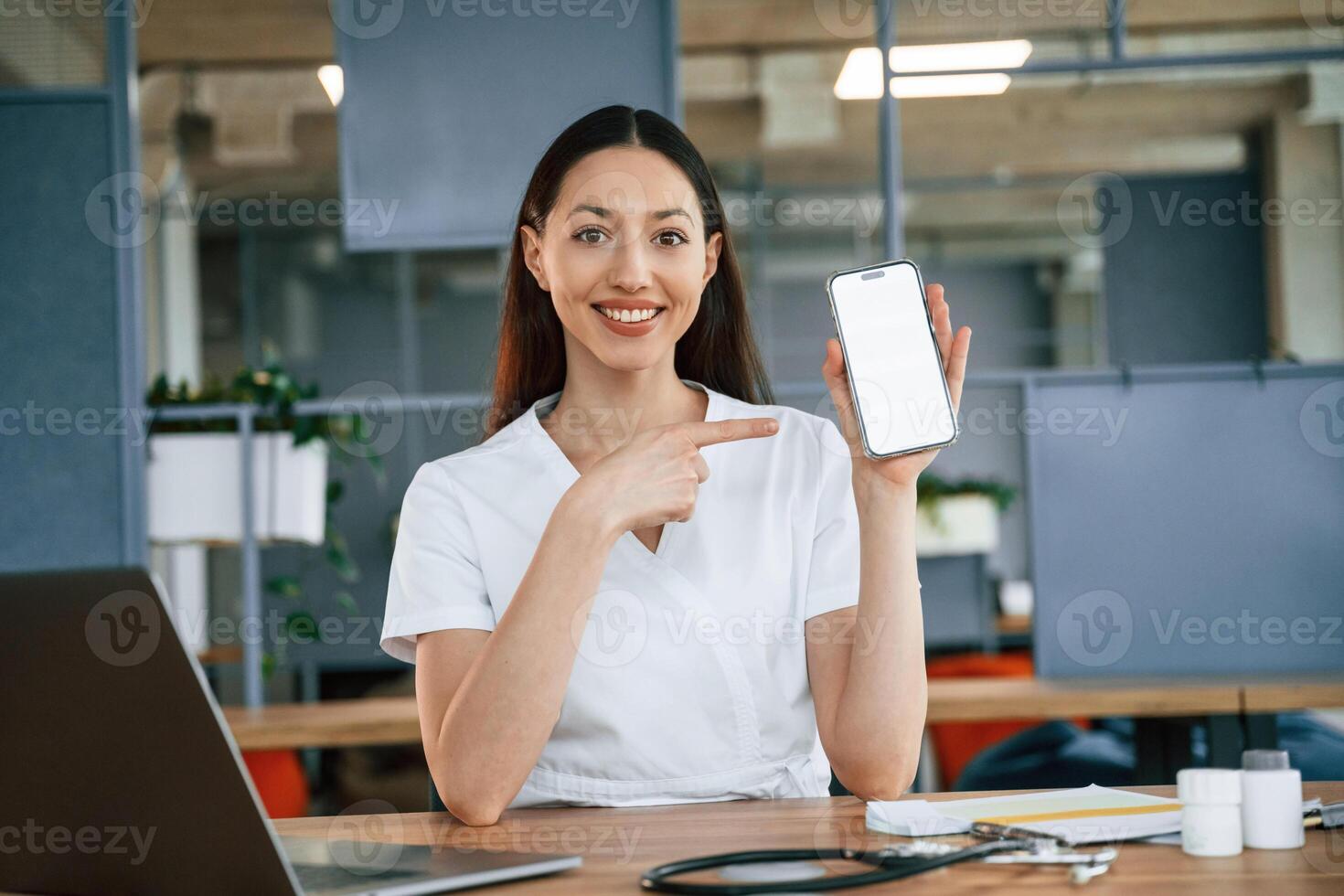 Holding smartphone ,with ,copy space on display. Female doctor in white coat is indoors photo