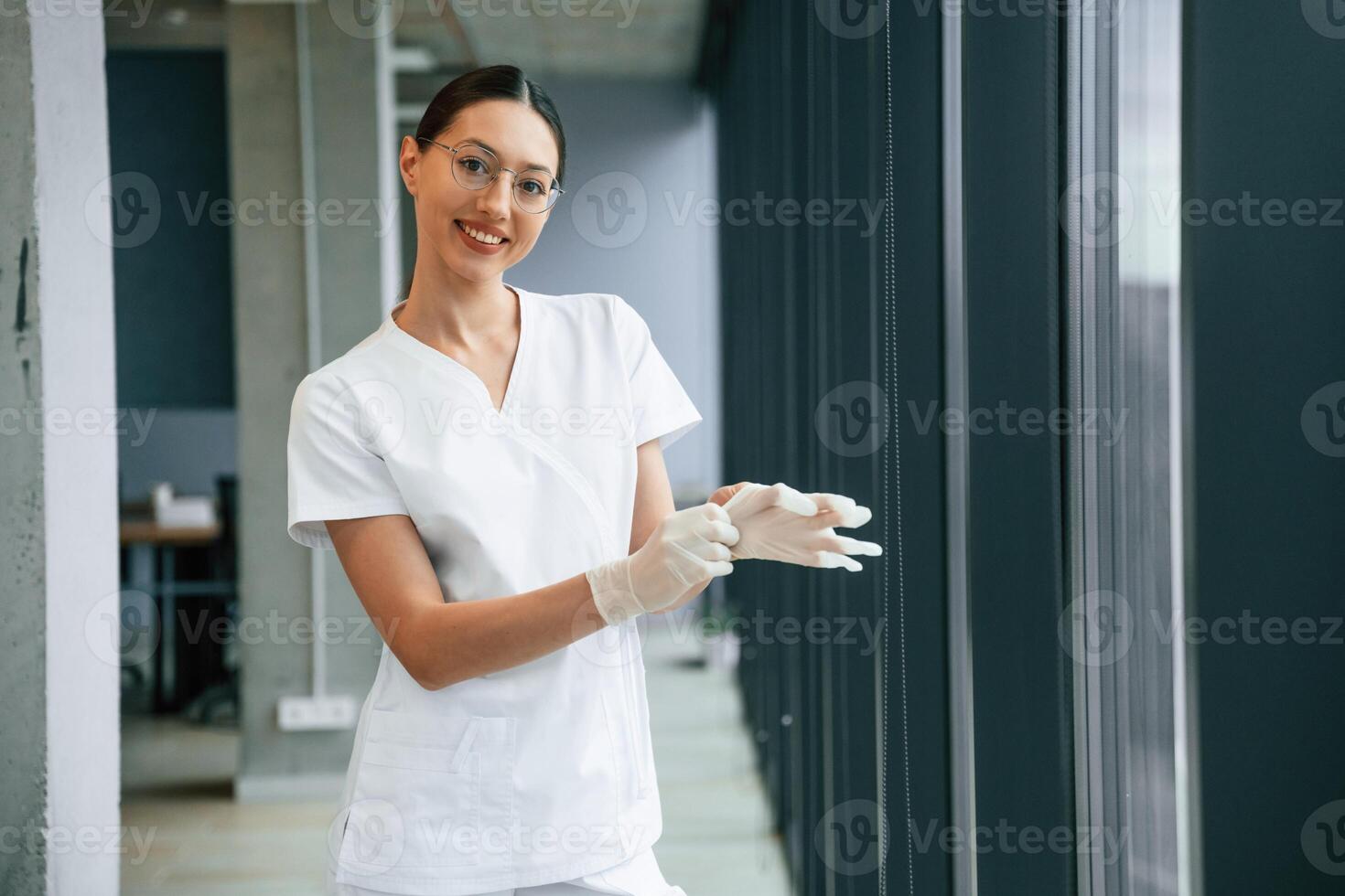 Preparing,, for work, wearing gloves. Female doctor in white coat is indoors photo