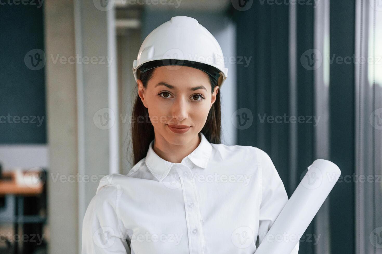 Portrait ,,of female architect that is in hard hat and in white clothes indoors photo