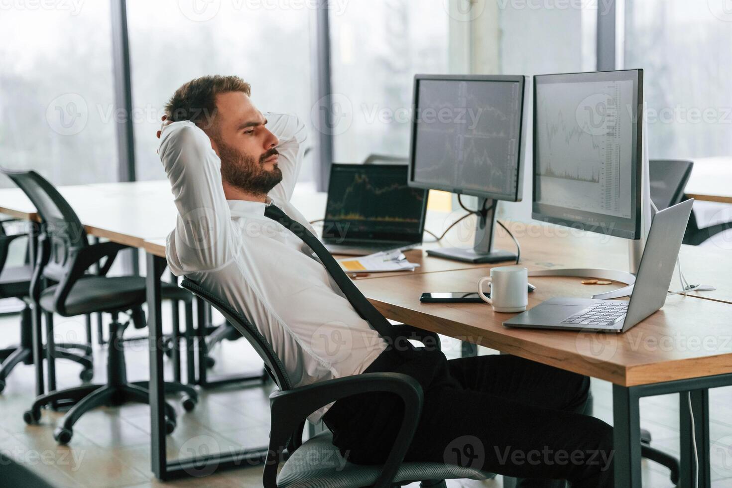 Sitting, with ,hands behind the head. Businessman is by computer and working in the ,office photo