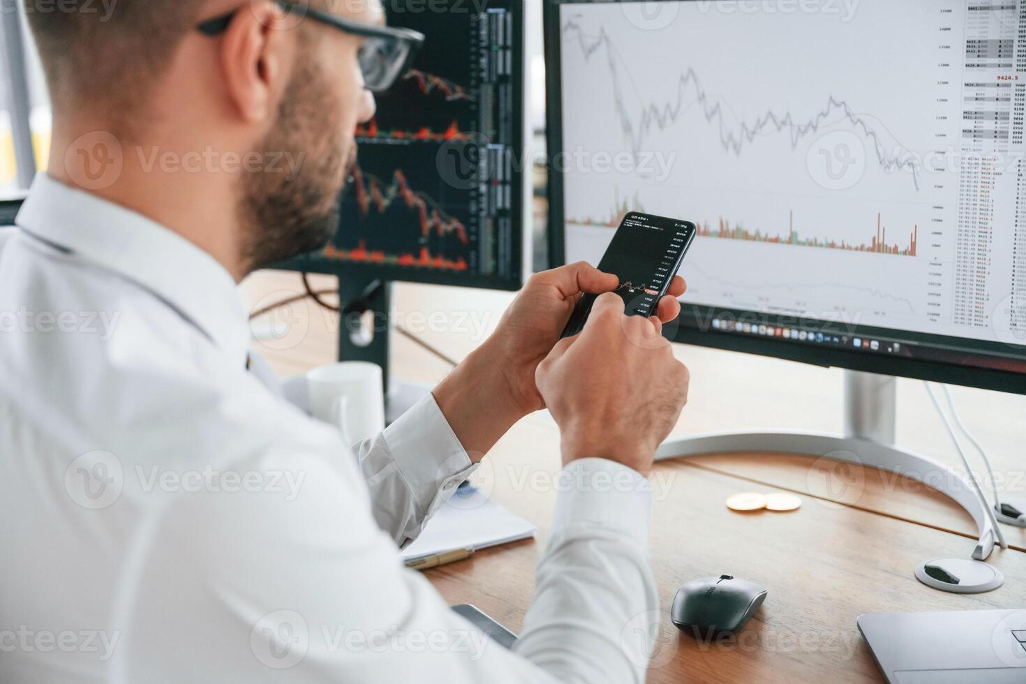 Holding smartphone in hands. Businessman is sitting by computer and working in the, office photo