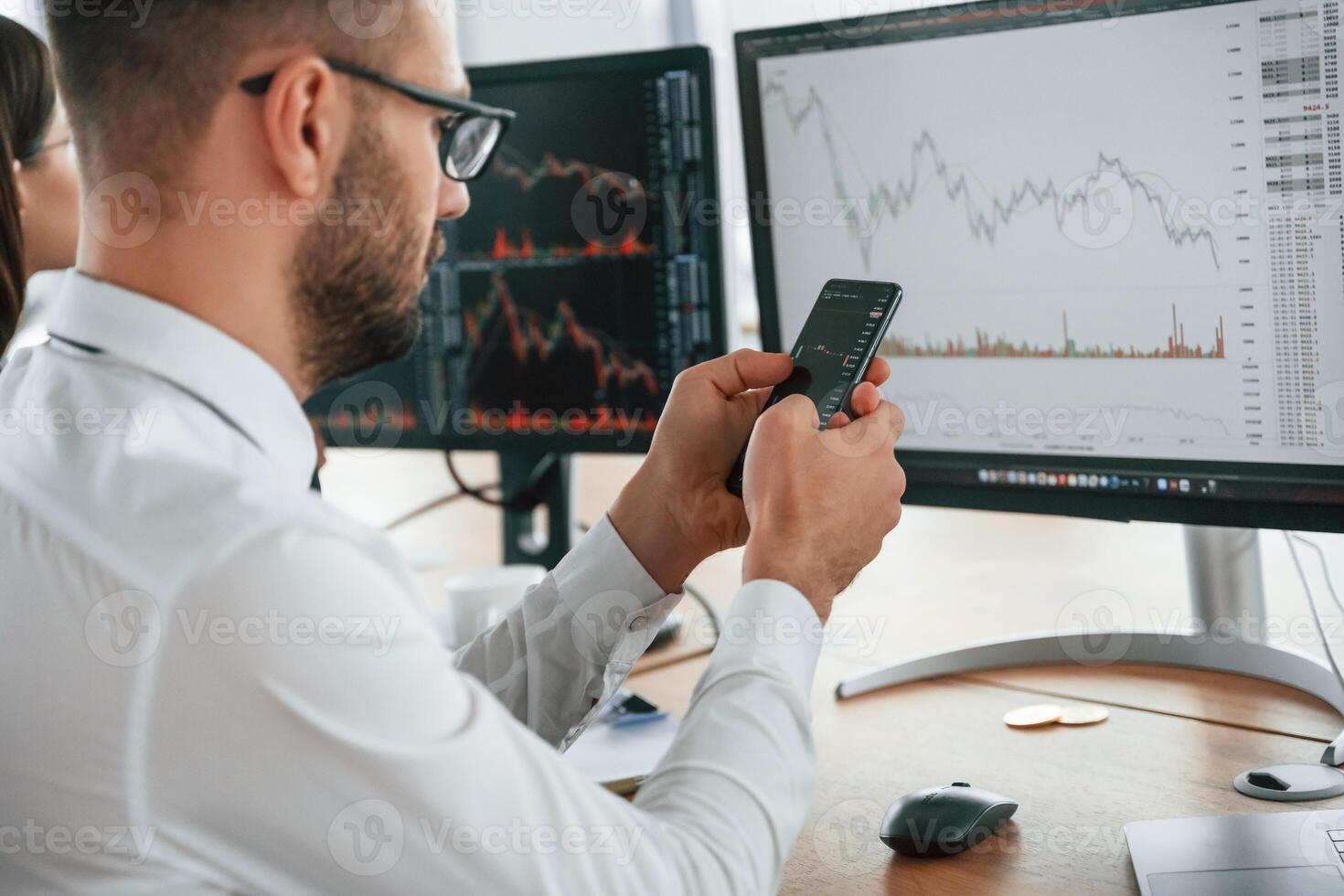 Holding, smartphone in hands. Businessman is sitting by computer and working in the office photo