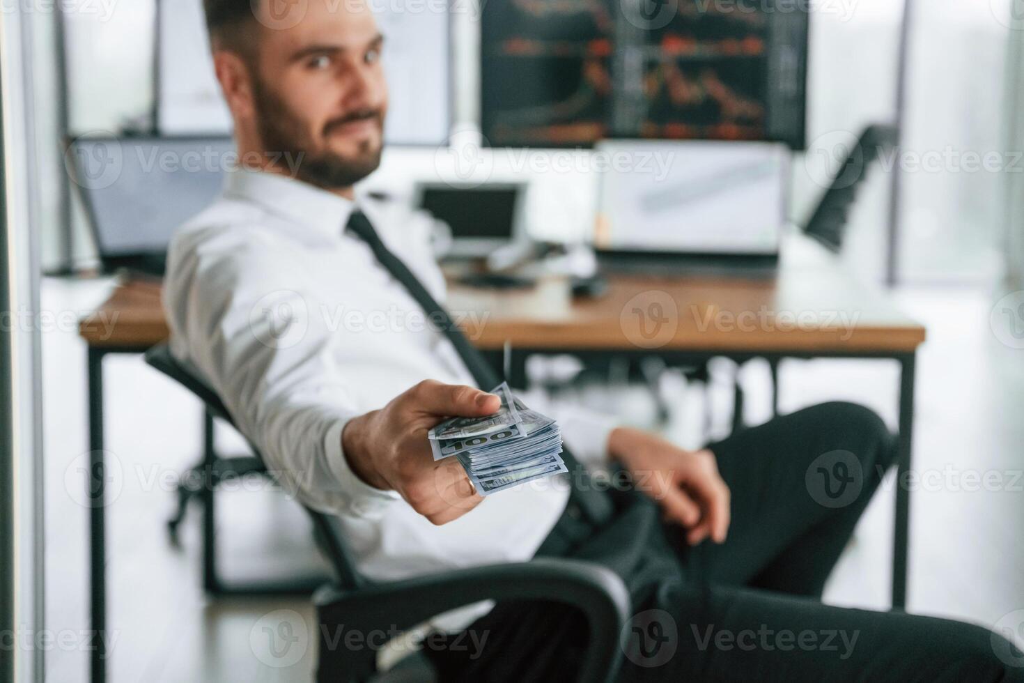 Giving lot, of, money. Holding in hand. Businessman is sitting by computer and working in the office photo