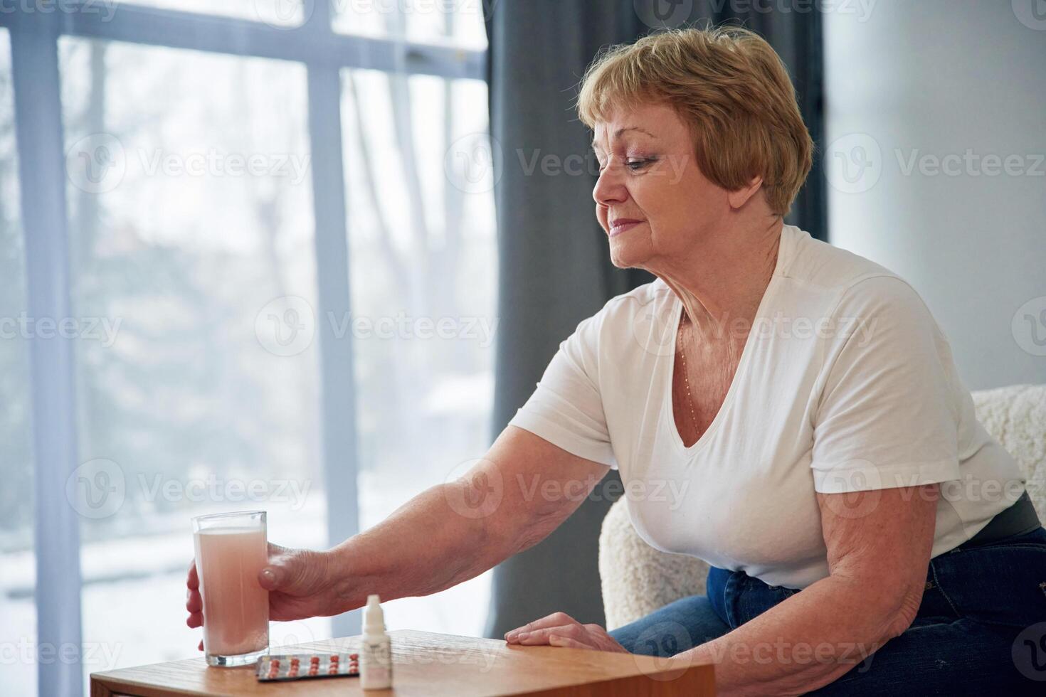 Drink, with anti flu medicament. Senior elderly woman is at home in the living room photo