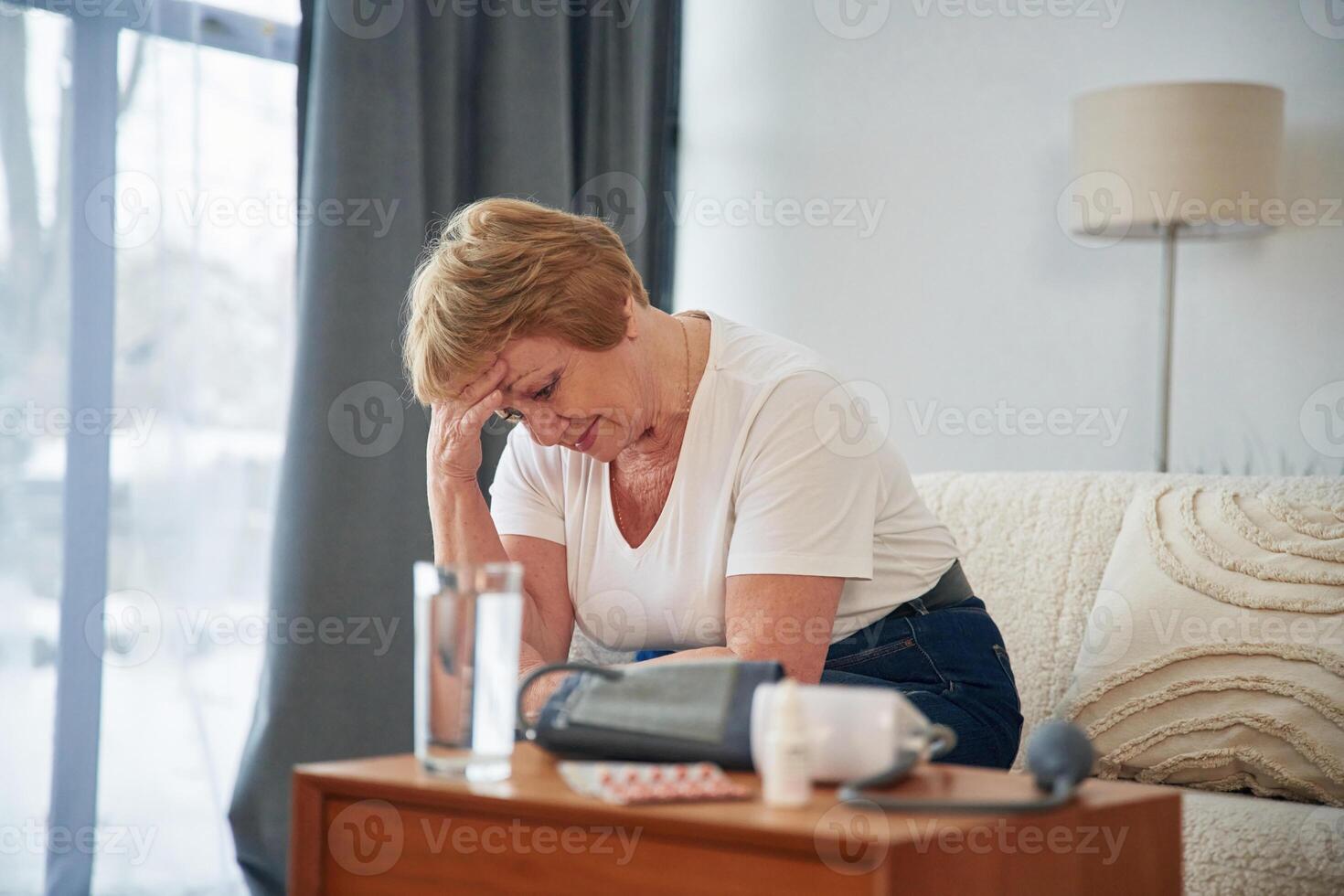 Feeling, bad, pills and ,blood measurement equipment. Senior elderly woman is at home in the living room photo