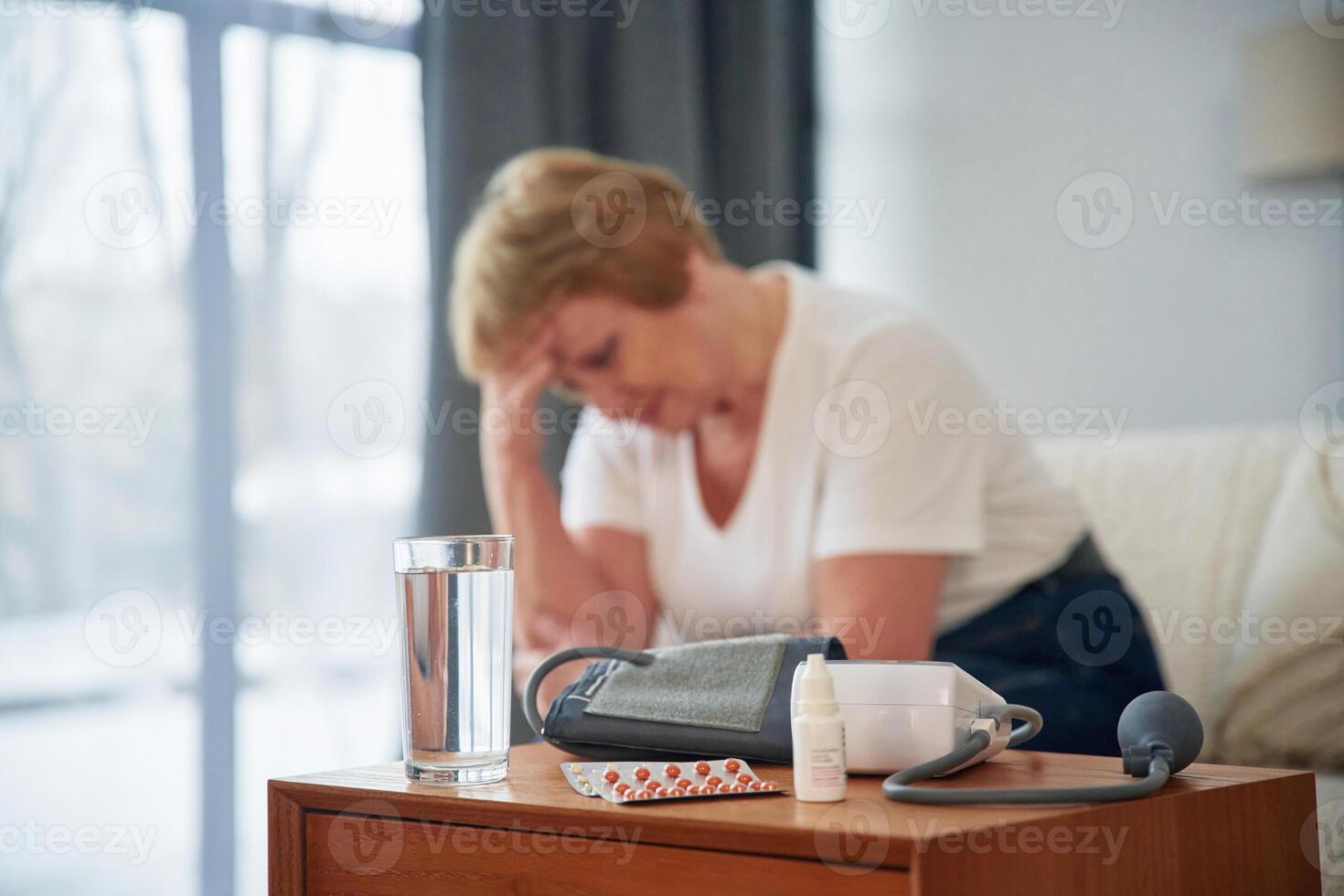 Sick, feeling bad. Pills on the table. Senior elderly woman is at home in the living room photo