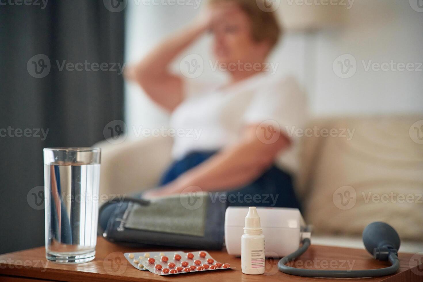 Feeling bad, pills and, blood measurement equipment. Senior elderly woman is at home in the living room photo