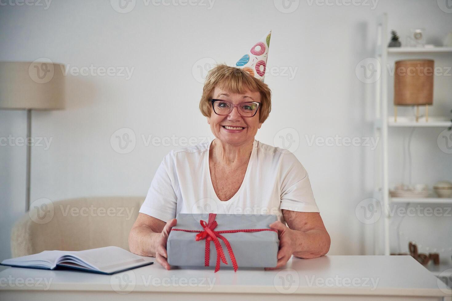 Celebrating, birthday. With,, gift in the present box. Senior elderly woman is at home in the living room photo