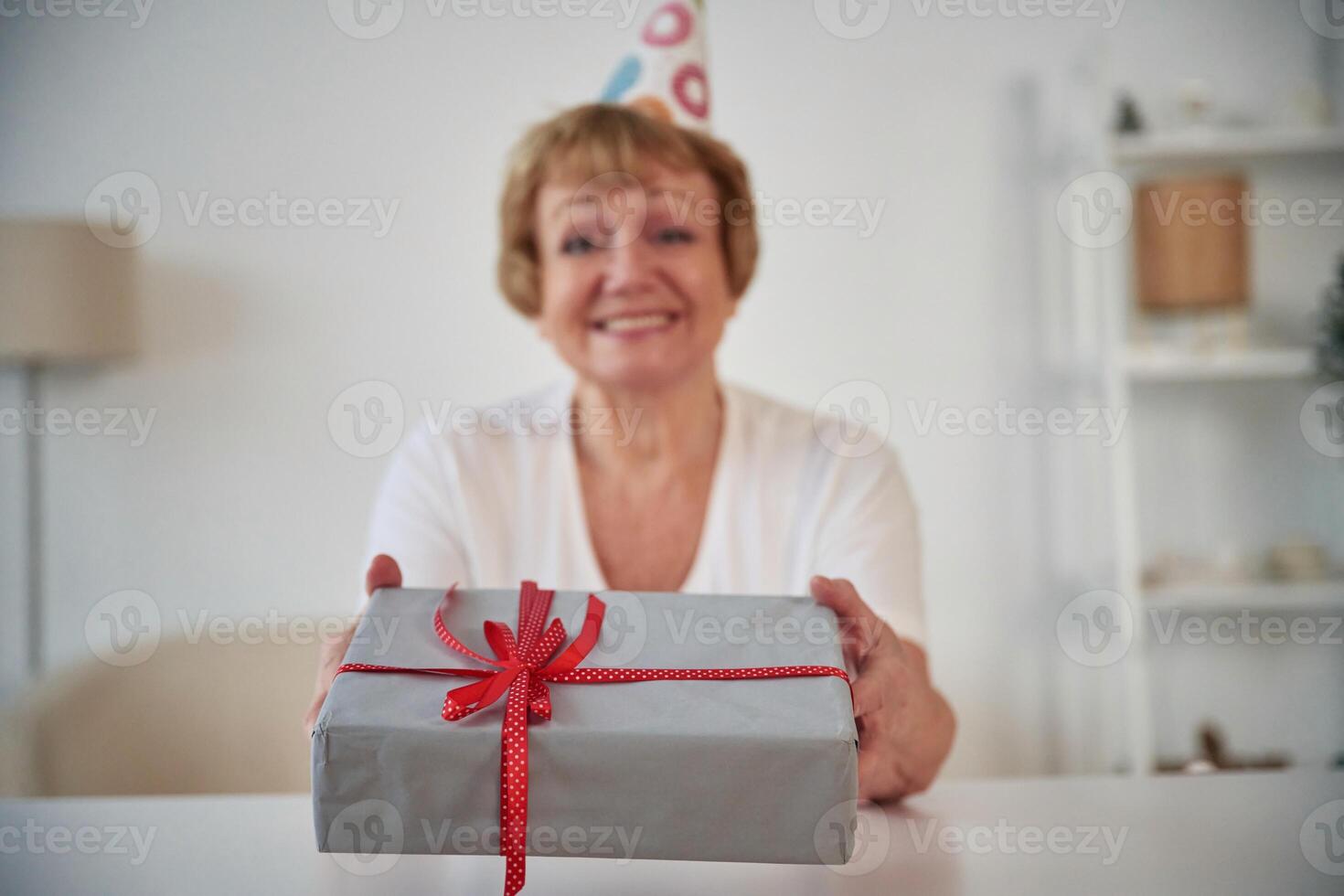 Smiling,, celebrating birthday, holding gift box. Senior elderly woman is at home in the living room photo