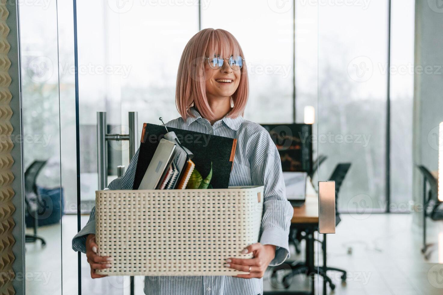 Standing and smiling,. Unemployed woman with pink hair is with personal belongings after being fired photo