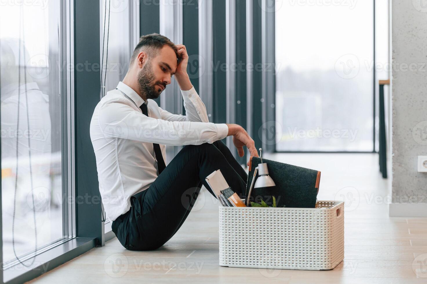 Feeling bad, sitting, on floor. Unemployed man is with personal belongings after being fired photo