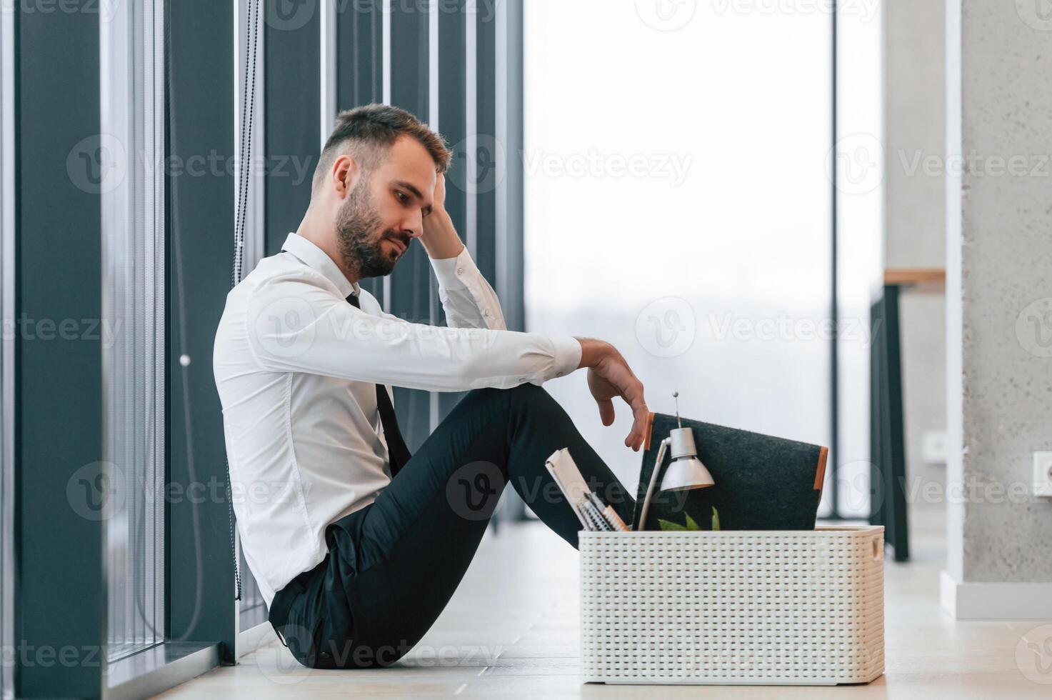 Feeling bad,, sitting on floor. Unemployed man is with personal belongings after being fired photo