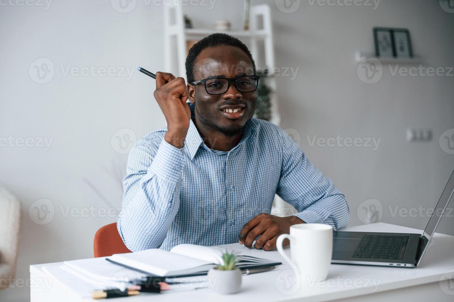 Sitting and smiling. With ,pen ,in hand. Businessman is working in the office by laptop photo