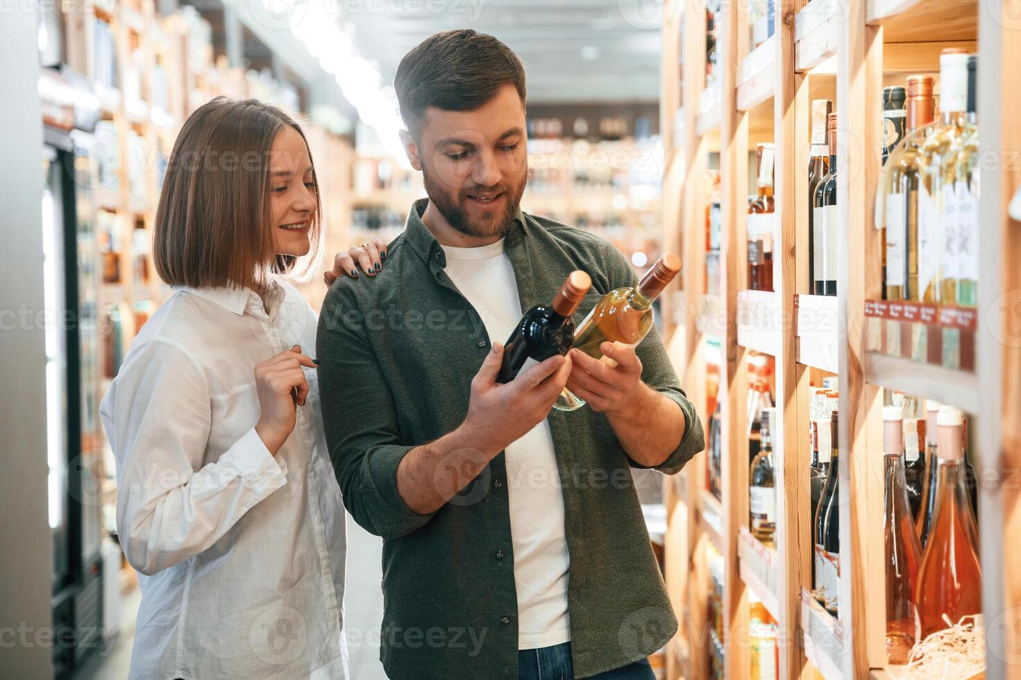 Choosing between two ,different bottles. Man and woman in the wine shop photo