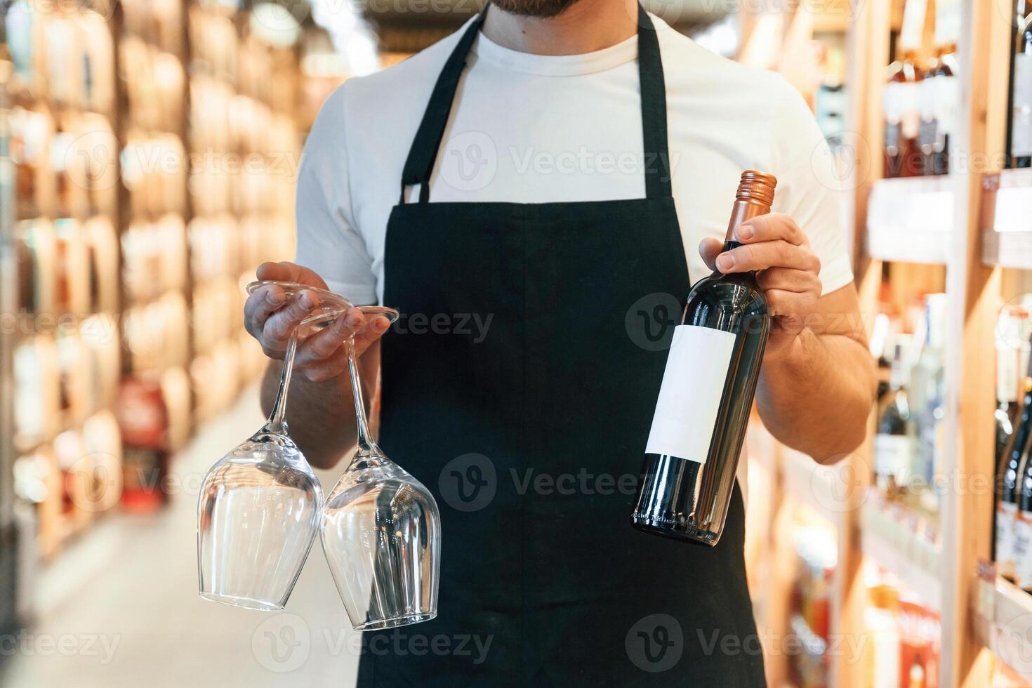Two, glasses and bottle in hands. Wine shop owner in white shirt and black apron photo