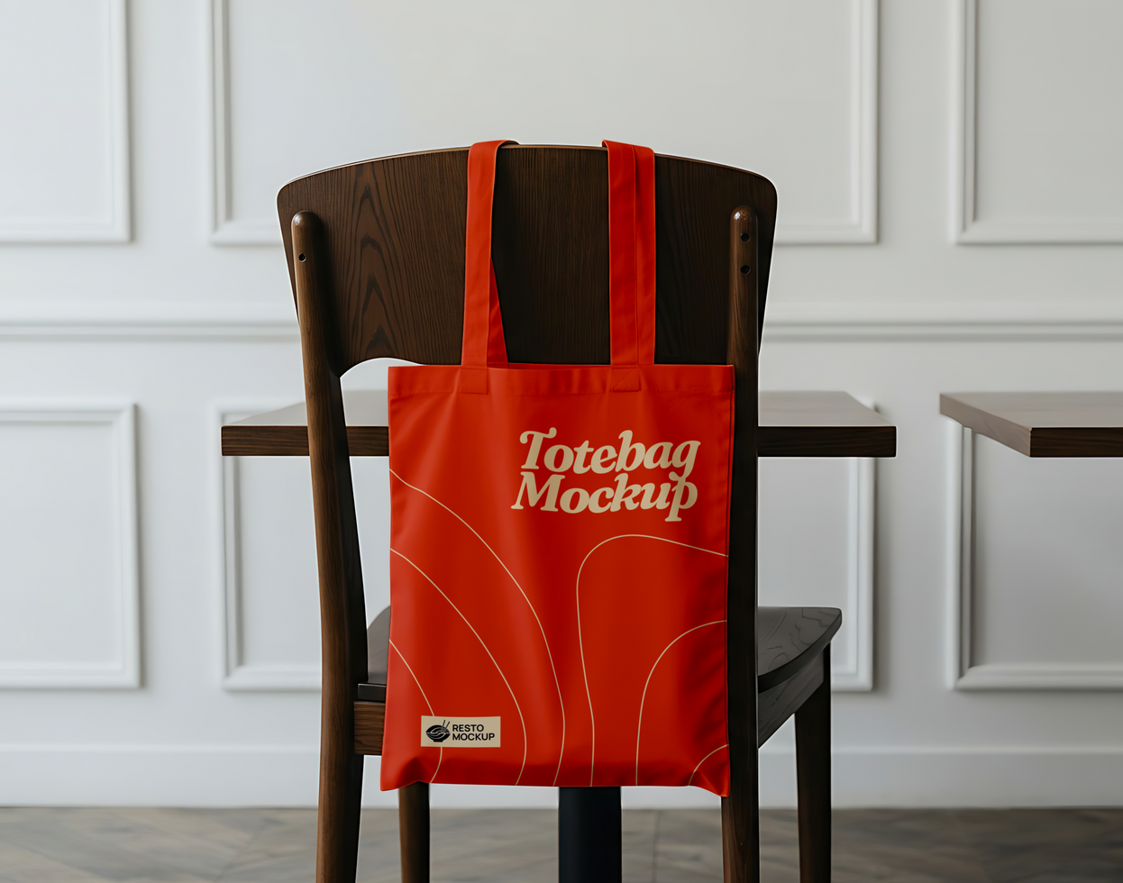 A red tote bag mockup hangs on the back of a wooden chair psd