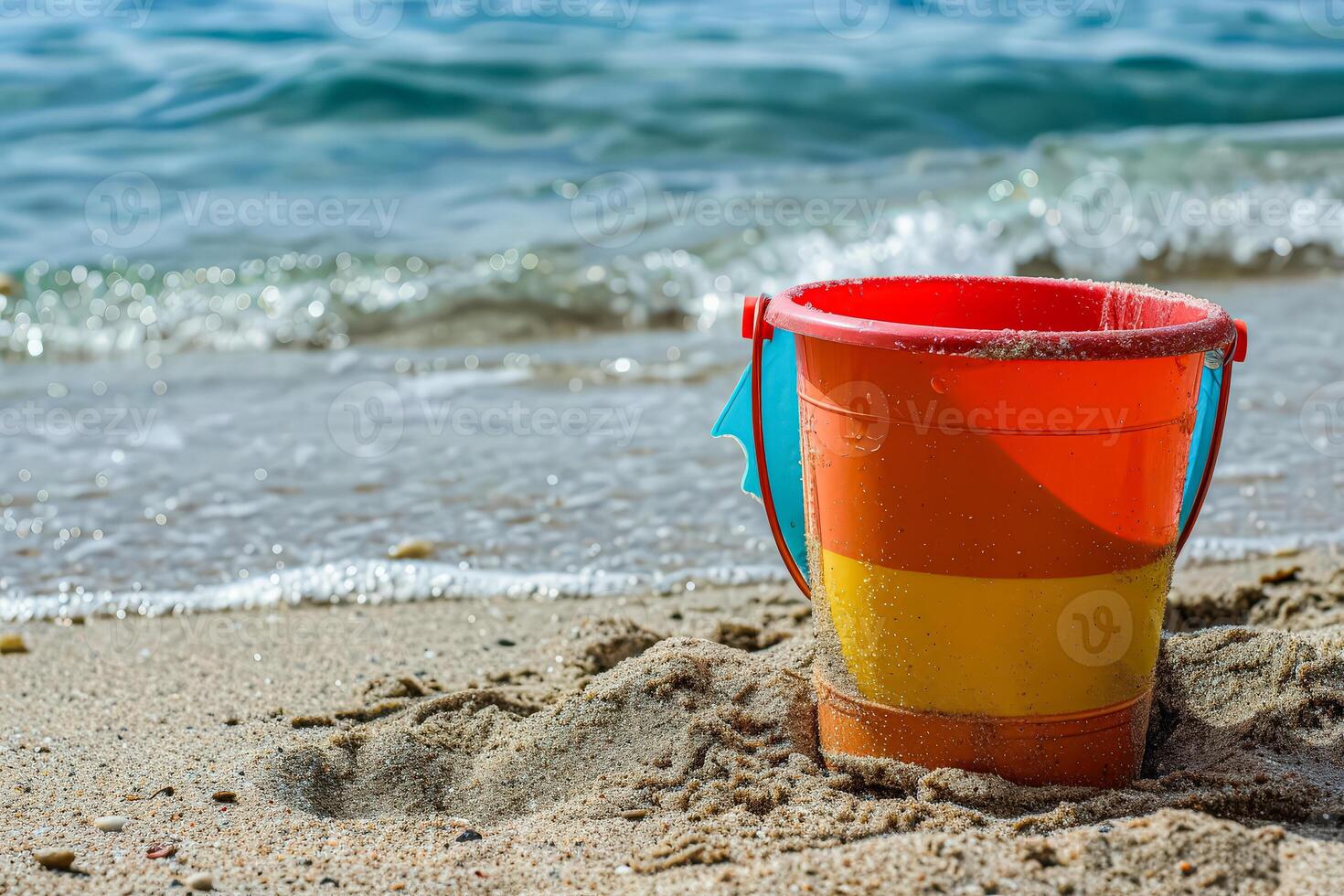 Red and yellow bucket is sitting on the sand at the beach photo