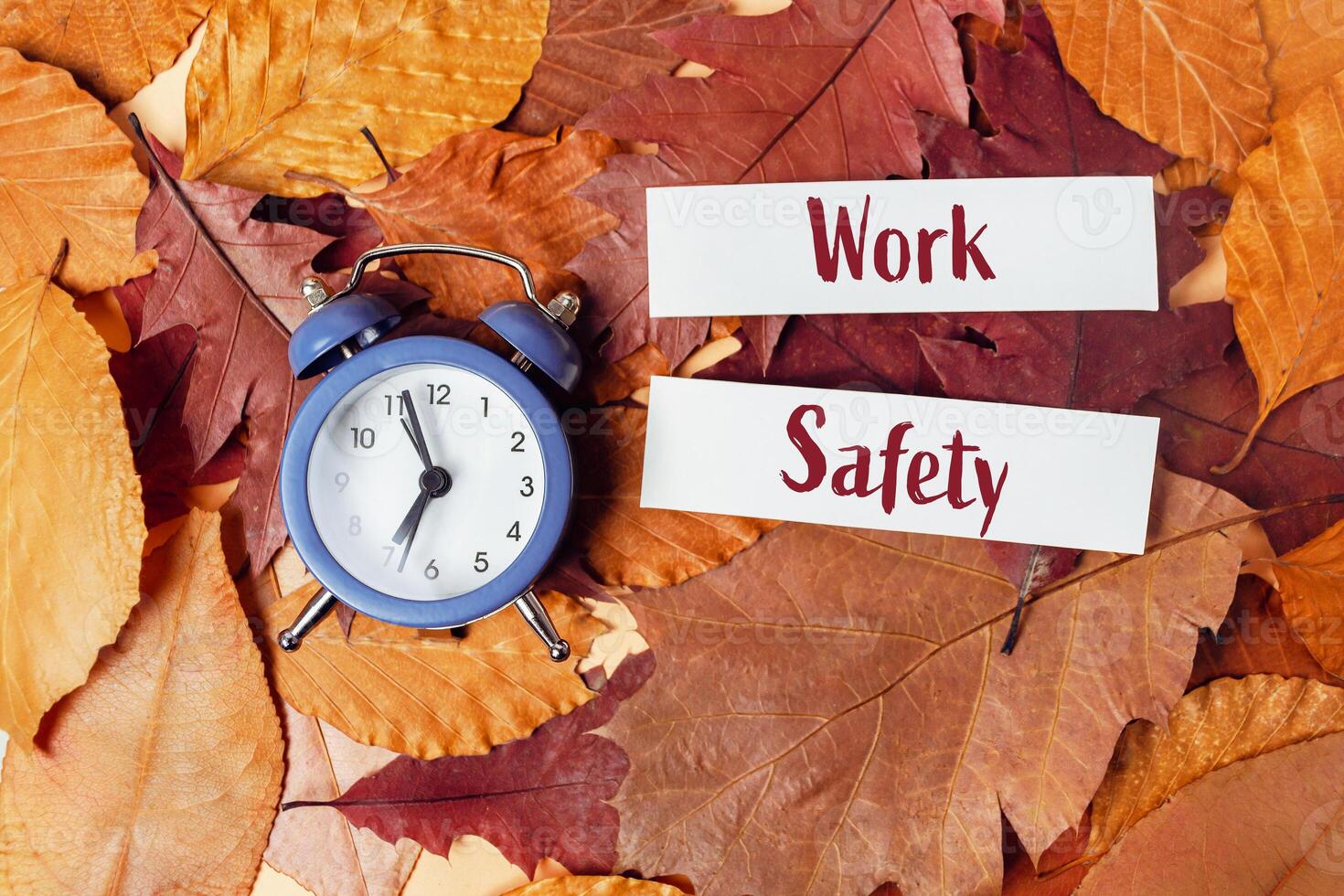 Blue alarm clock is on top of pile of orange leaves photo