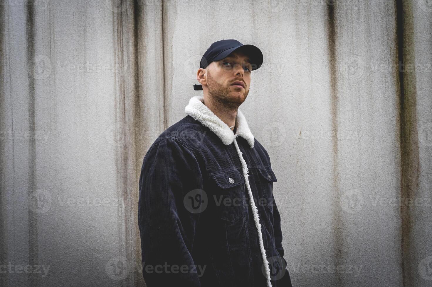 young rapper with black hat posing in front of a white wall photo