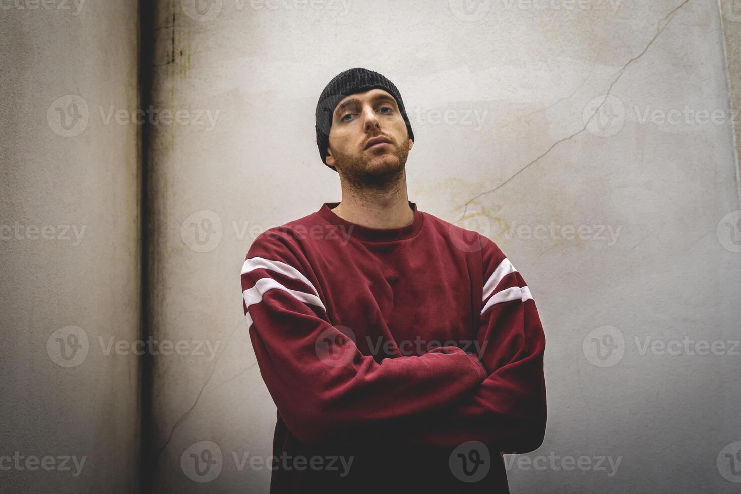 young rapper with arms crossed in front of a dirty wall photo