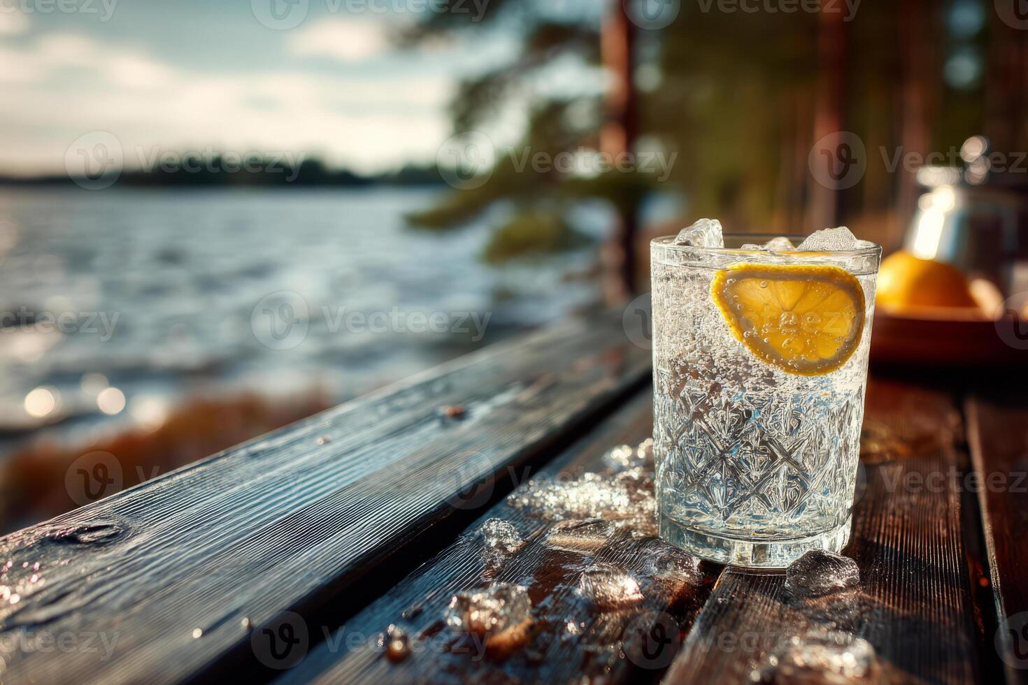 Glass of lemon water with ice on wooden pier by lake photo