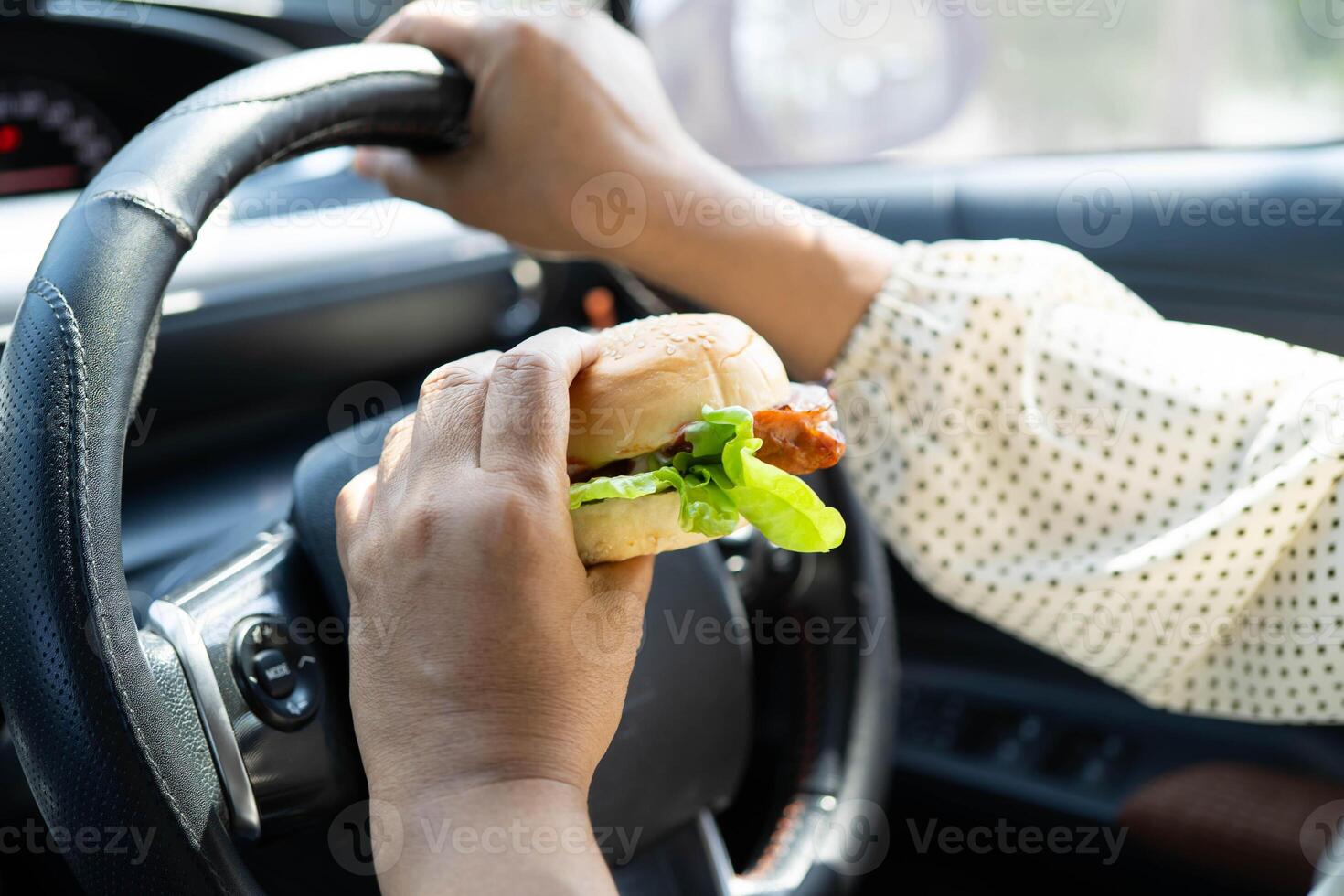 Asian woman driver hold and eat hamburger in car, dangerous photo