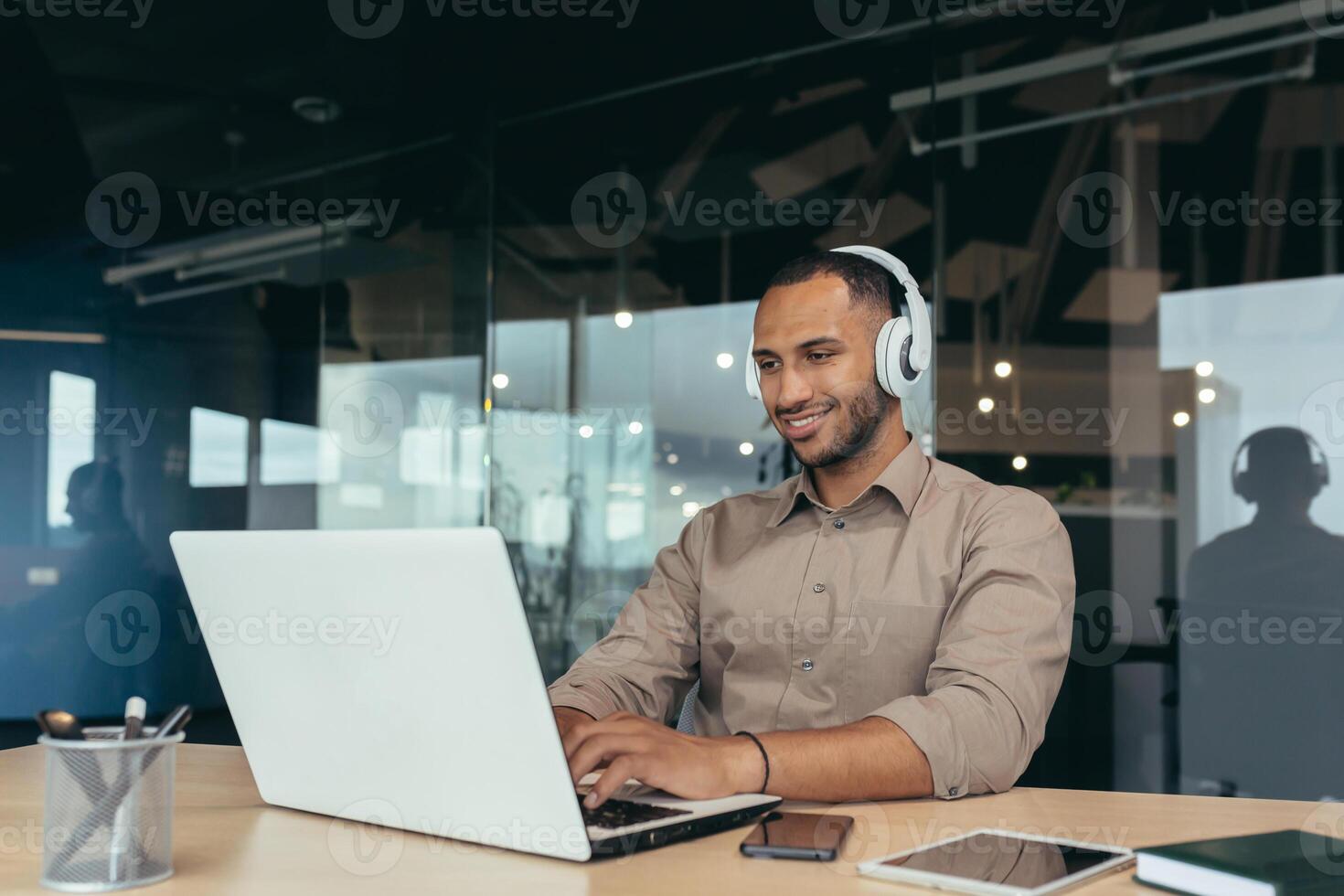 Young office worker working inside office building, using laptop to watch and headphones, businessman on break. photo