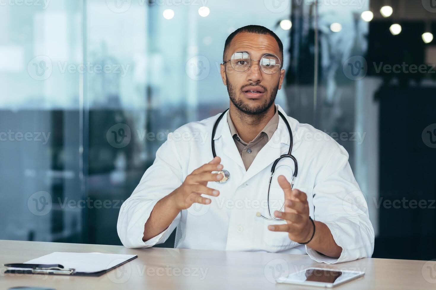 Serious and focused doctor in medical coat and stethoscope talking on call looking at camera and consulting patient, man working inside clinic office. photo