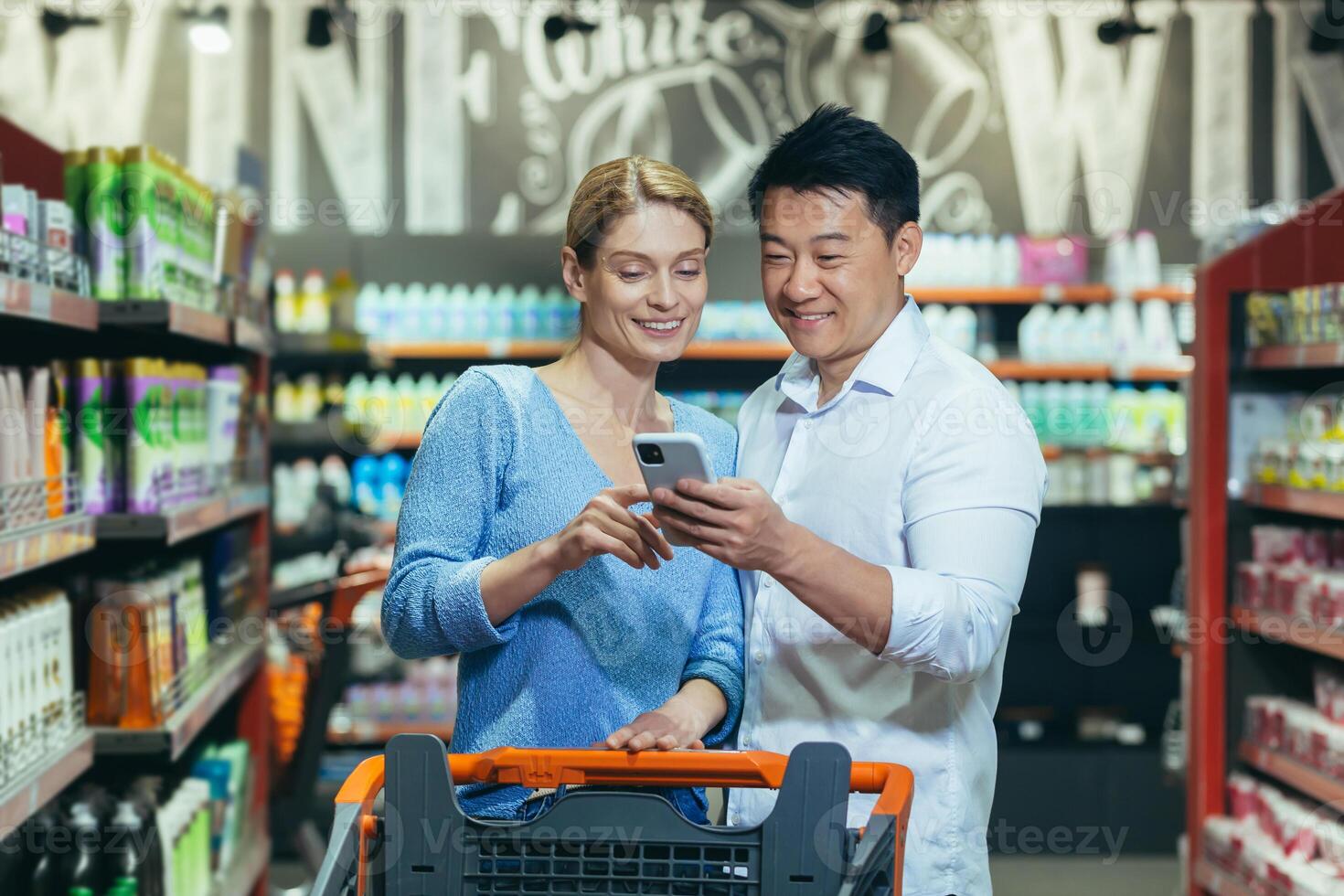 Happy couple of shoppers in supermarket, using phone to compare shopping list, man and woman shopping together photo