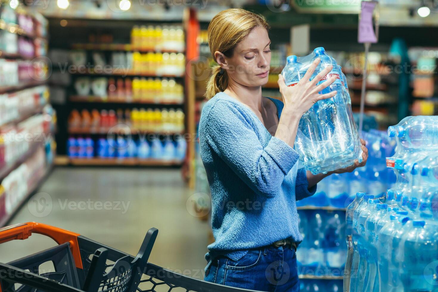 A frightened and sad woman in a crisis buys water in a supermarket, stocks up on drinking water photo