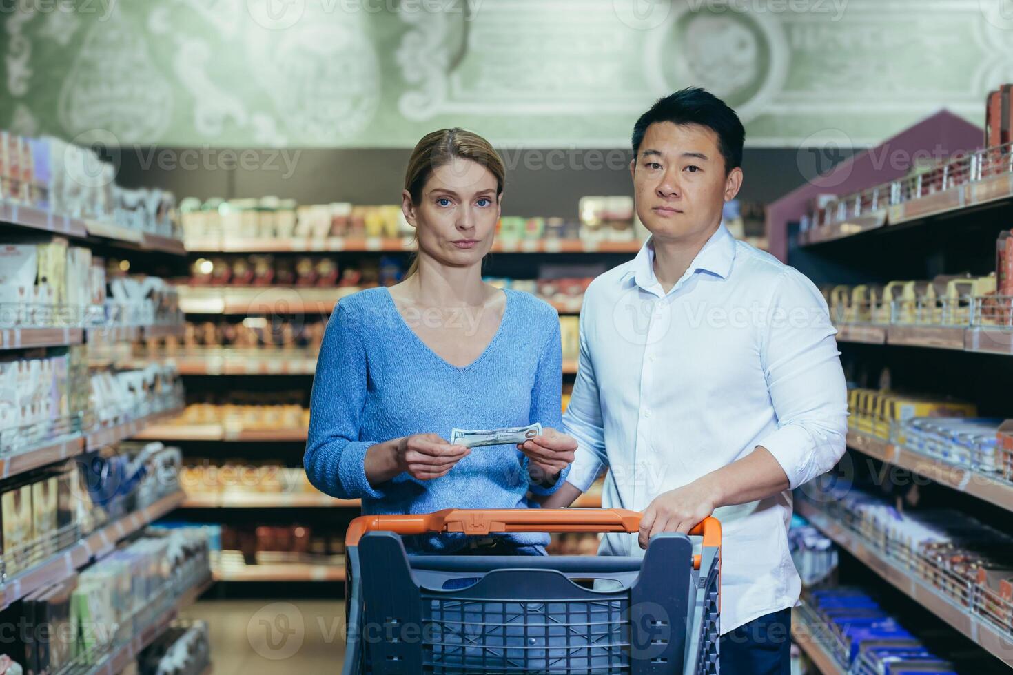 Upset young couple in supermarket, man and woman looking at camera poor have no opportunity and money to shop, multiracial family. photo