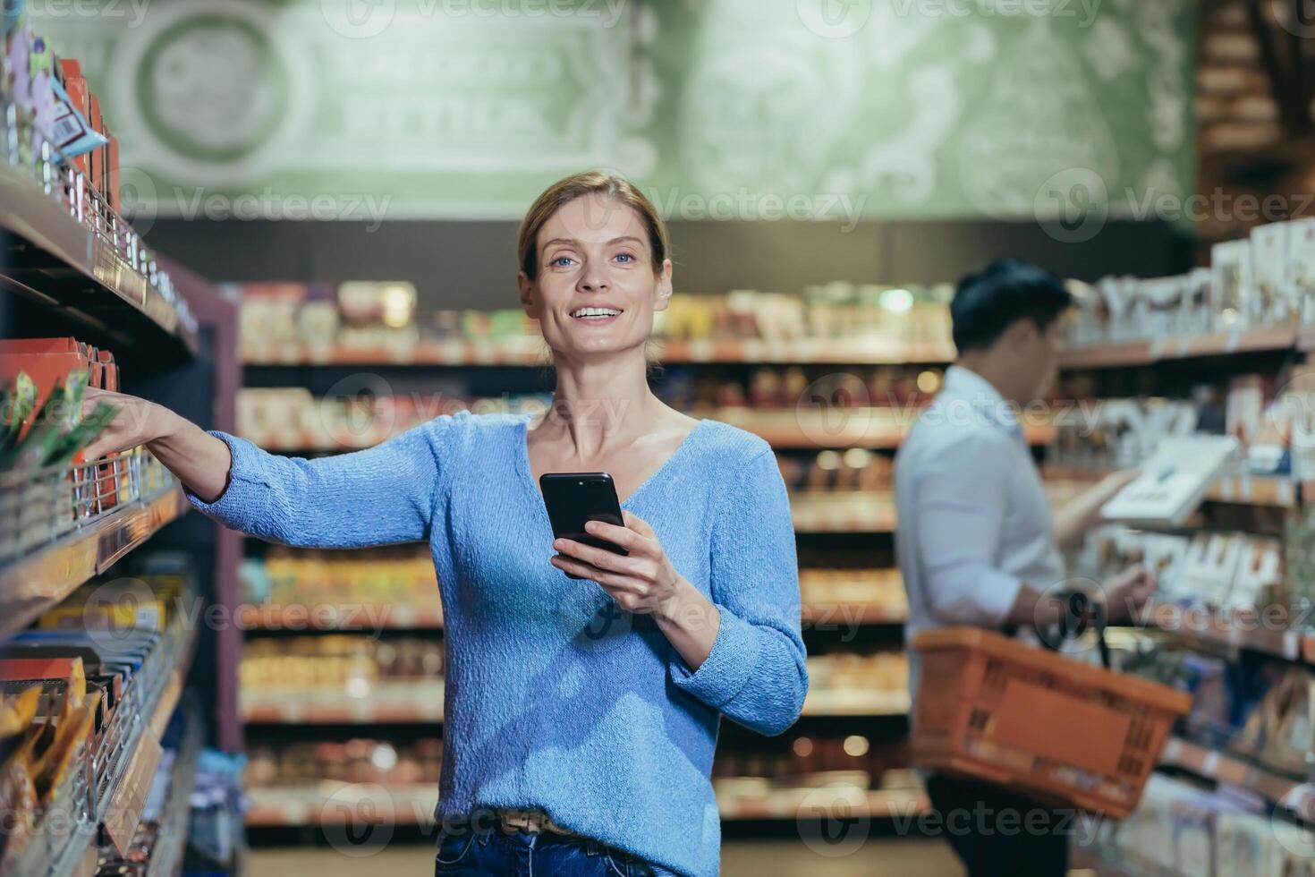 Portrait of a woman buyer in a supermarket in the grocery department, a blonde housewife chooses goods and makes purchases looking at the camera and smiling. photo
