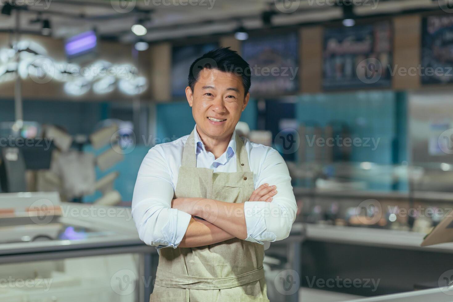 portrait of handsome asian man salesman in apron standing and looking at camera in grocery store supermarket. Male worker seller or small business owner. indoor. food, groceries market Cheerful smile photo