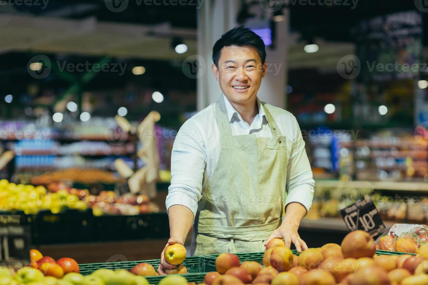 Portrait of Asian supermarket salesman, man in grocery vegetable section smiling and looking at camera. photo