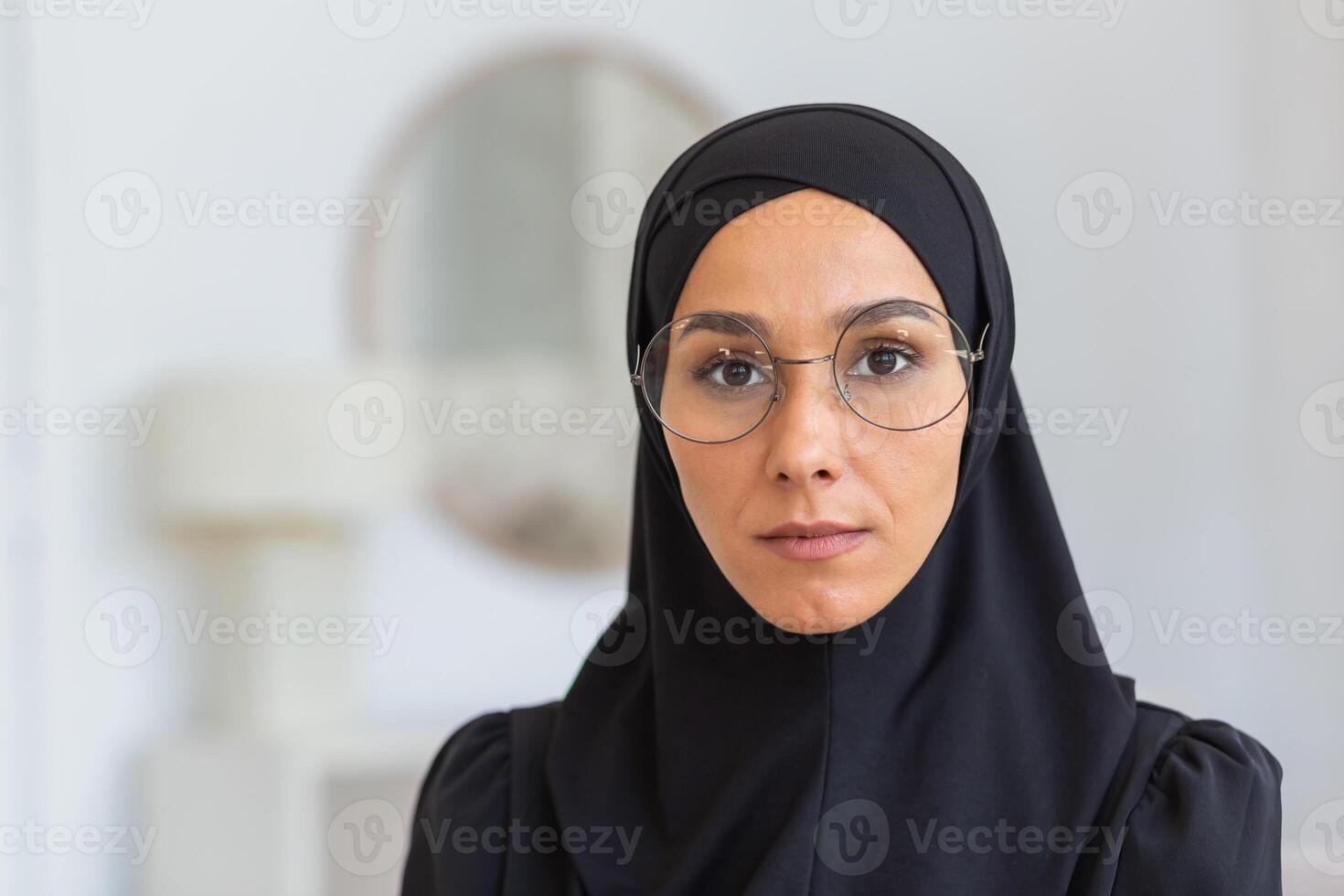 Close-up photo. Portrait of a young woman, an immigrant, a refugee from eastern countries, wearing a black hijab and glasses, looking seriously into the camera. photo