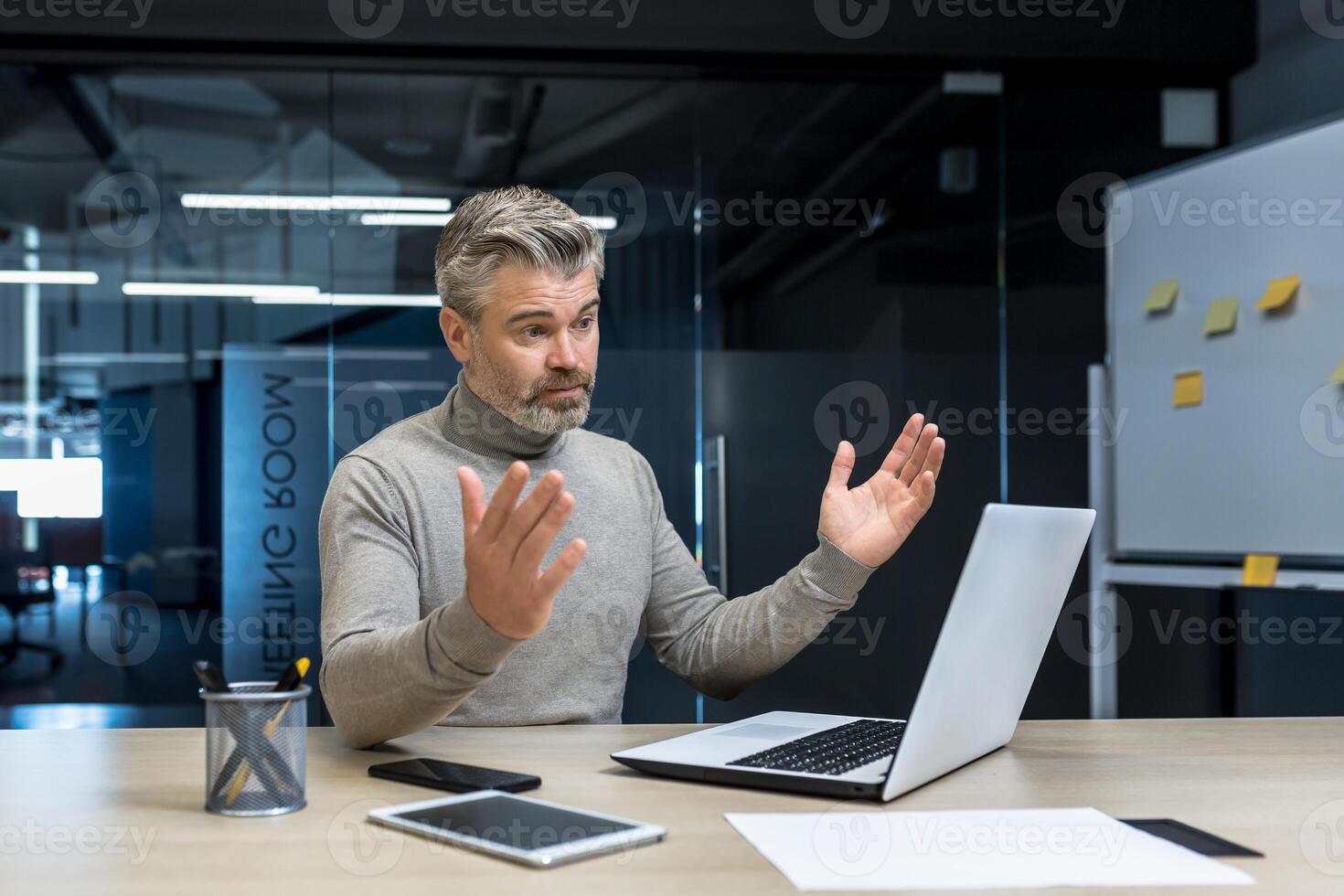 Frustrated and upset gray-haired experienced businessman, mature man spreading hands, negative work result, senior businessman at work using laptop photo