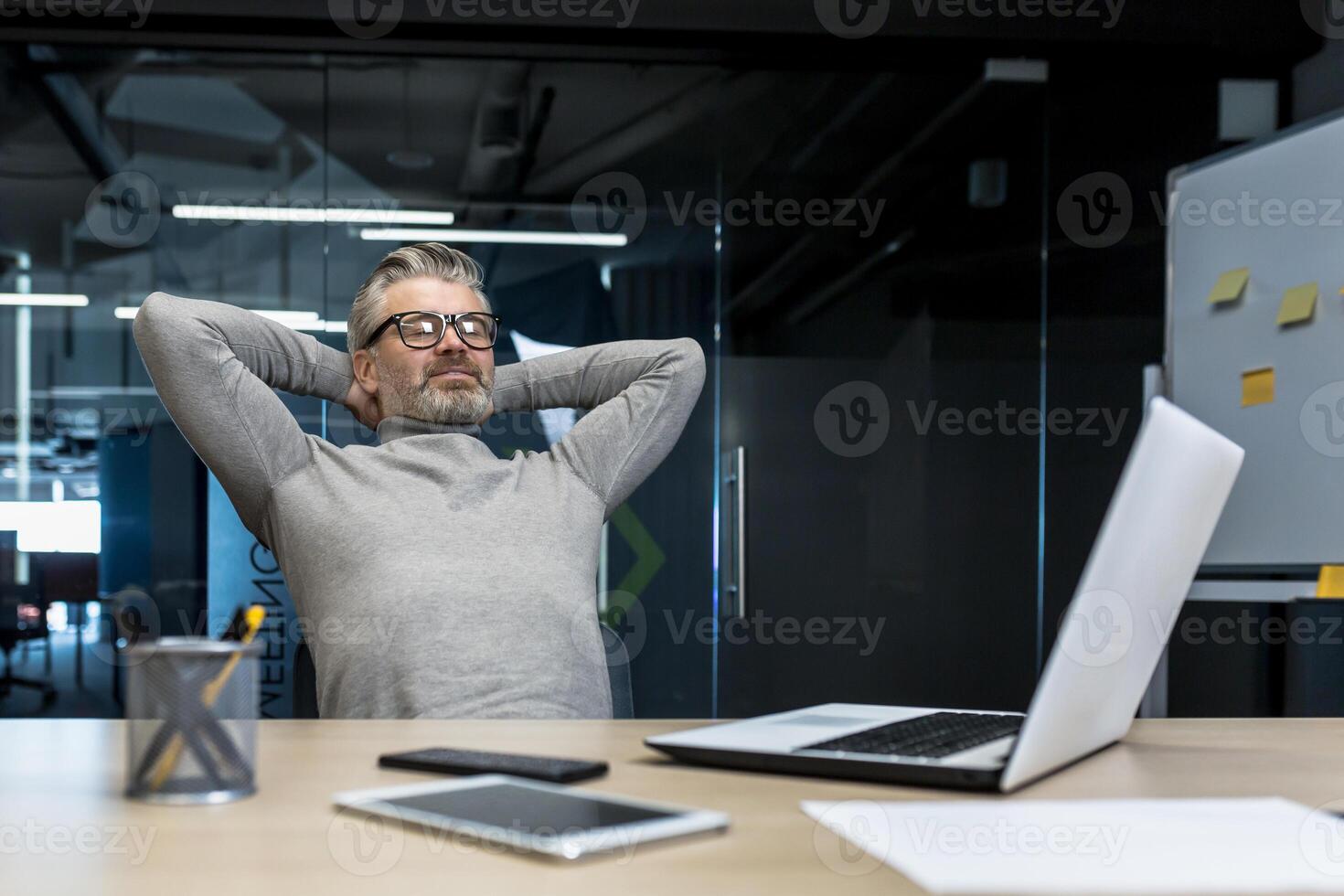 Senior gray haired man resting in office on chair with hands behind head, businessman boss working using laptop, mature investor completed project, dreaming. photo