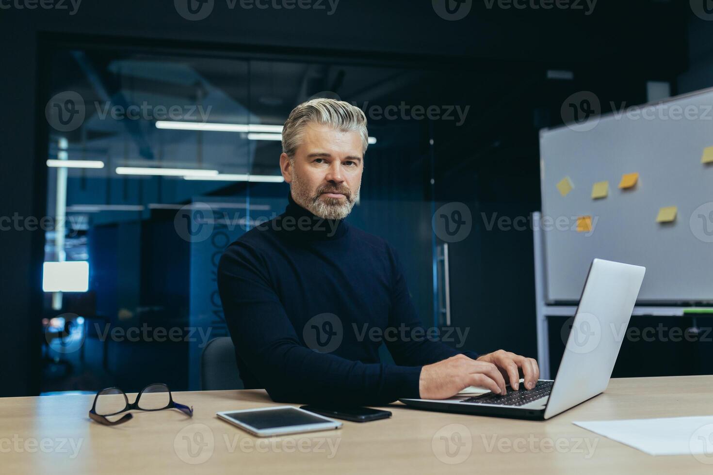 Portrait of serious gray haired boss, man looking at camera thinking, mature businessman inside office working at desk using laptop at work. photo