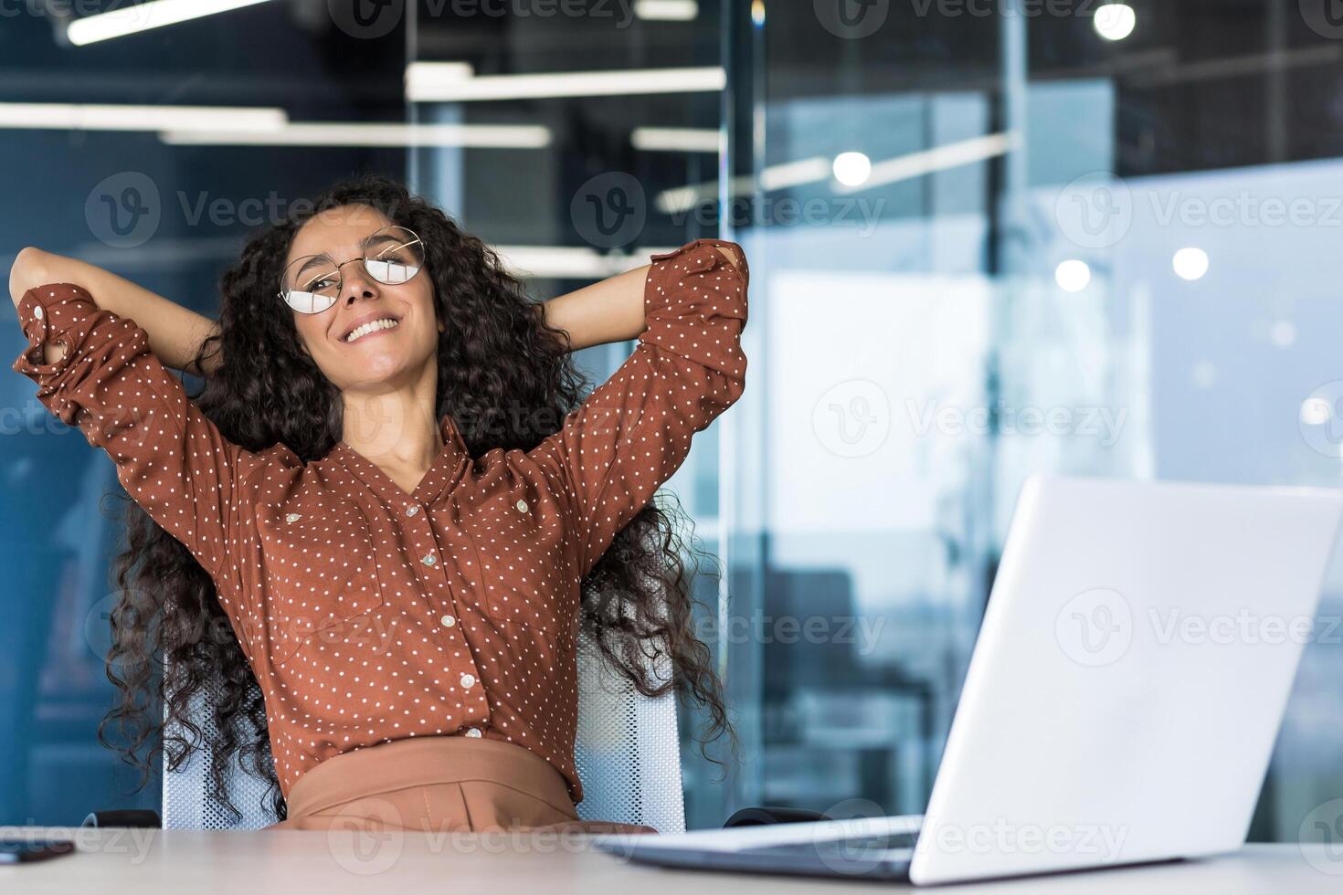 Young woman engineer developer programmer works in the office inside the IT company, satisfied with the work result, rests hispanic looks out the window, smiles hands behind her head, dreams. photo