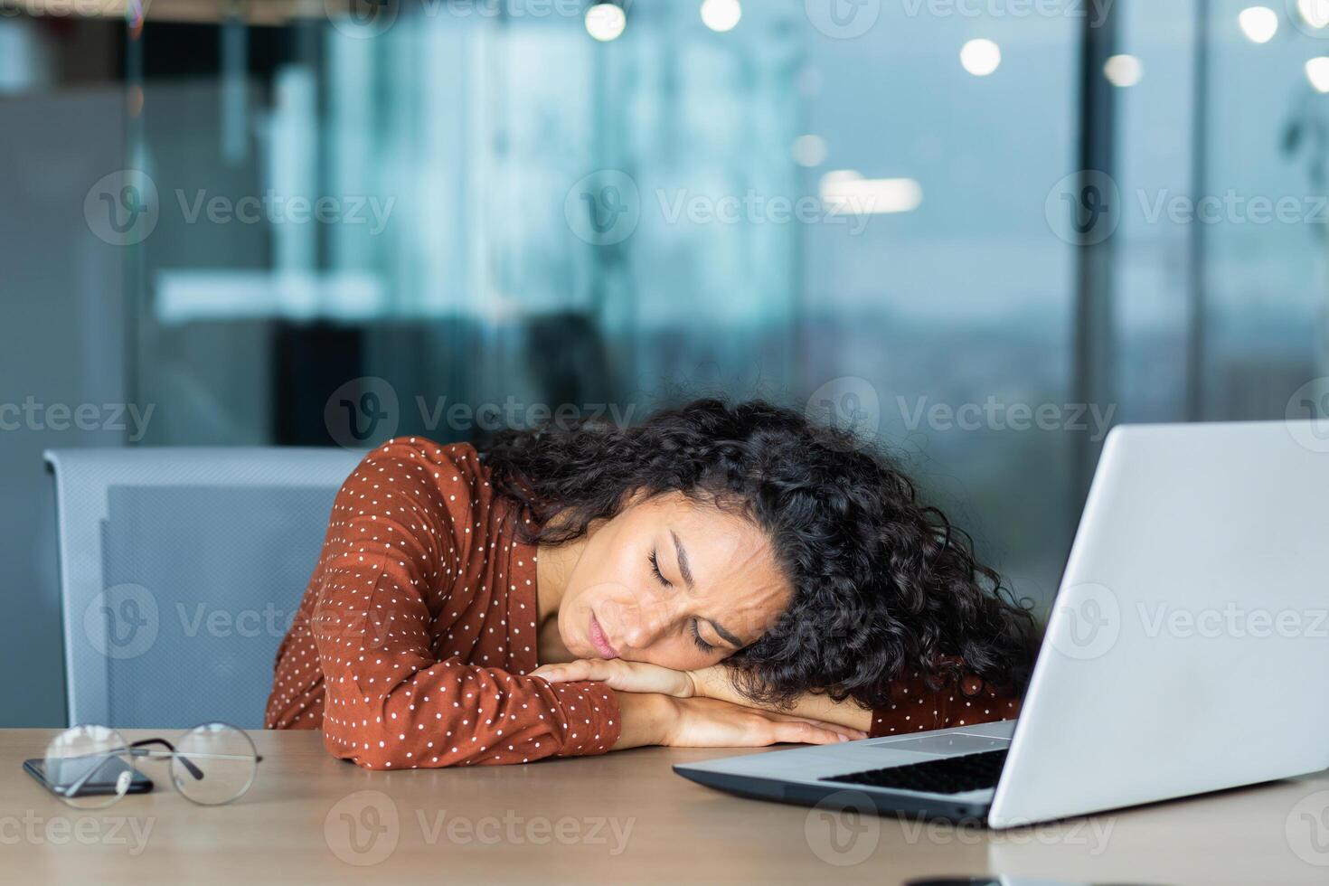 Beautiful tired hispanic woman sleeping on desk, close-up business woman with closed eyes napping inside office near laptop. photo