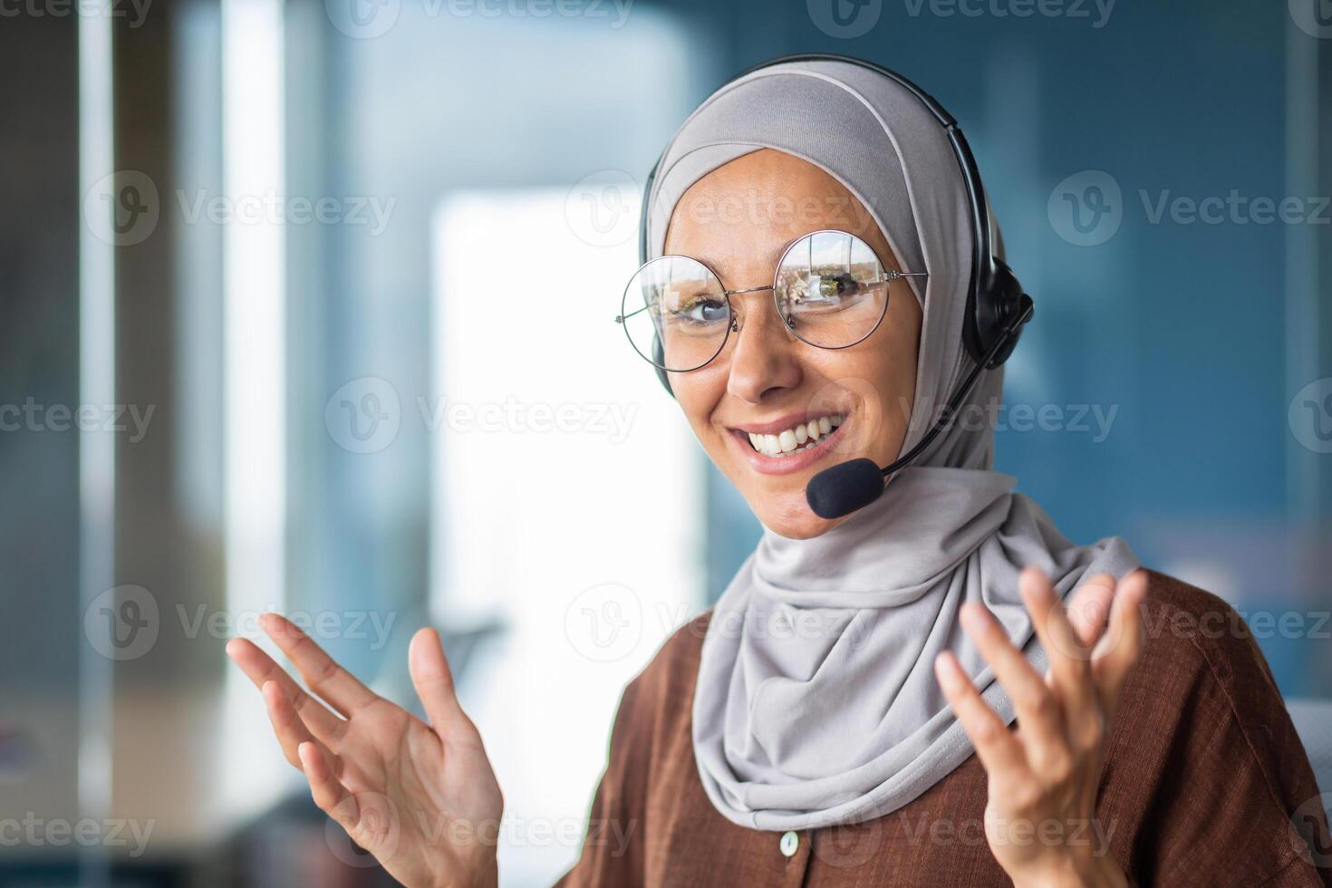 Portrait of young Muslim woman teacher in hijab and headset, conducting online training. He smiles at the camera, gestures with his hands. Close-up photo. photo
